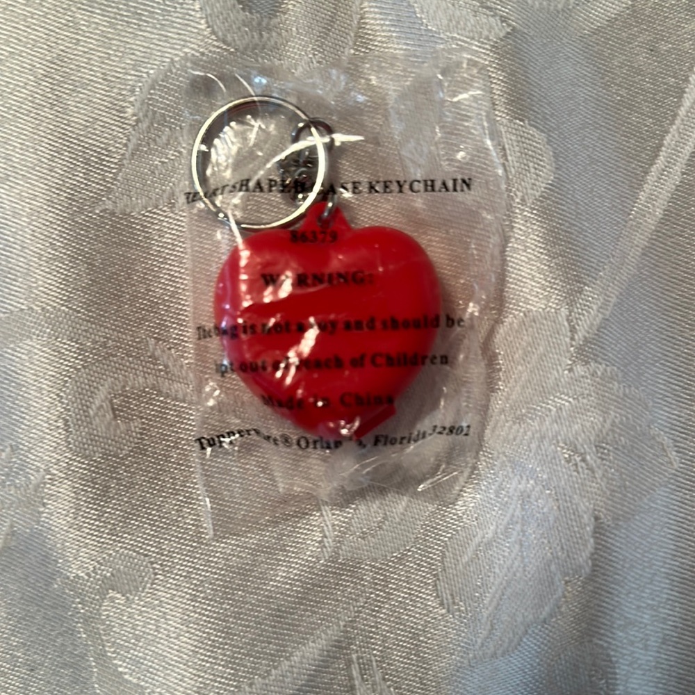 New in bag heart shaped keychain with lid that snaps closed.